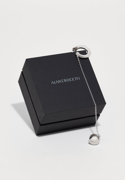 Cutie de bijuterii neagră cu un lanț argintiu atașat de un accent spherical. Cutia are un logo imprimat într-un font modern.
