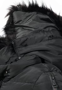 Chaqueta de invierno acolchada negra con ribete de piel sintética en la capucha, cierres visibles de cremallera y botones a presión, tejido liso y ligeramente brillante.