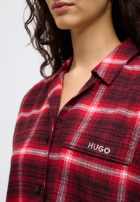 Κόκκινο και μαύρο πουκάμισο φλάναλ με καρό μοτίβο και γιακά, με λευκές ρίγες, μαύρα κουμπιά και κεντημένο λογότυπο "HUGO" στην τσέπη στο στήθος.