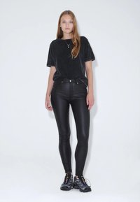 Černé oversized bavlněné tričko s měkkou strukturou, doplněné o černé vysoké skinny džíny z imitace kůže a robustní tenisky.