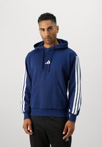 Felpa con cappuccio blu navy realizzata in tessuto morbido, dotata di tasca frontale, cappuccio con cordino e design a tre strisce bianche sulle maniche. Piccolo logo sul petto.