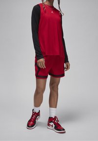 Punainen urheilullinen toppi mustien pitkien hihojen päällä, yhdistettynä punaisiin shortseihin, joissa on mustia yksityiskohtia, sekä punaisiin ja mustiin koripallokenkiin.