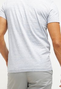 T-shirt court à manches courtes gris clair en tissu doux, avec une texture légèrement chinée. Design simple avec un col rond.