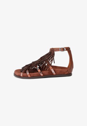 Sandale plate marron avec bride à la cheville, franges et détails cloutés, avec plusieurs fines lanières brillantes sur le pied.