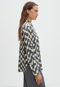 Long-sleeve shirt in beige with abstract dark gray pattern, featuring a collar and buttoned cuffs. Smooth, lightweight fabric with a loose fit.