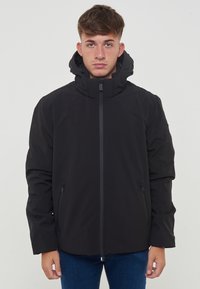 Giacca impermeabile nera con alto colletto e cappuccio rimovibile, dotata di una cerniera frontale e due tasche laterali. Textura liscia e opaca.