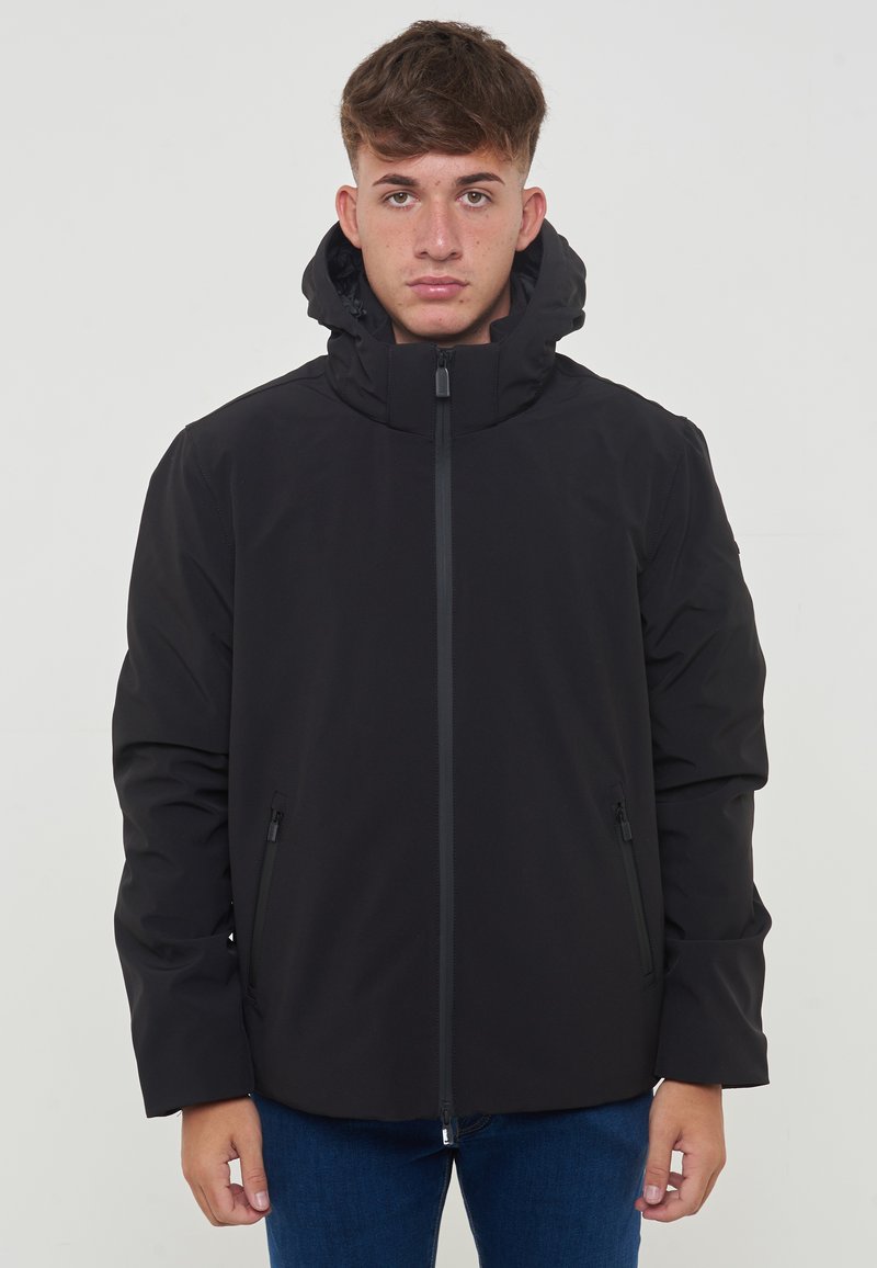 Giacca impermeabile nera con alto colletto e cappuccio rimovibile, dotata di una cerniera frontale e due tasche laterali. Textura liscia e opaca.