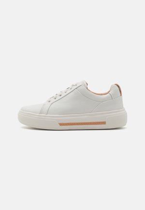 Sneaker de couro branco com um acabamento suave, bico arredondado e design de fecho minimalista. Apresenta um detalhe em bege na parte de trás e uma sola texturizada.