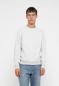 Halli sweatshirt ümmarguse kaelusega ja ribidega mansettidega, valmistatud pehmest puuvillasegus kangast, koos helesiniste teksadega.