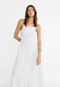 Weißes Maxikleid mit gerafftem Oberteil und gestuftem Rock. Verfügt über verstellbare Träger und einen fließenden, leichten Stoff.