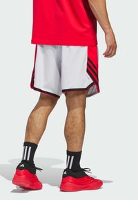 Punaiset urheilushortsit, joissa on valkoiset sivut, musta reunus ja kolme mustaa raitaa. Yhdistetty punaisiin kenkiin ja mustiin sukkiin, joissa on valkoisia raitoja.