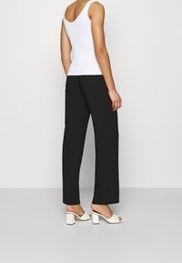 Top sin mangas blanco combinado con pantalones de pierna ancha negros y sandalias de tacón bloque blanco. Texturas suaves y diseño minimalista.