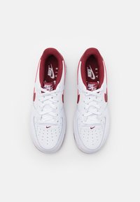 White Nike Air sneakers with red accents, featuring a perforated toe, flat laces, and branded insoles. Rubber sole with rounded shape.