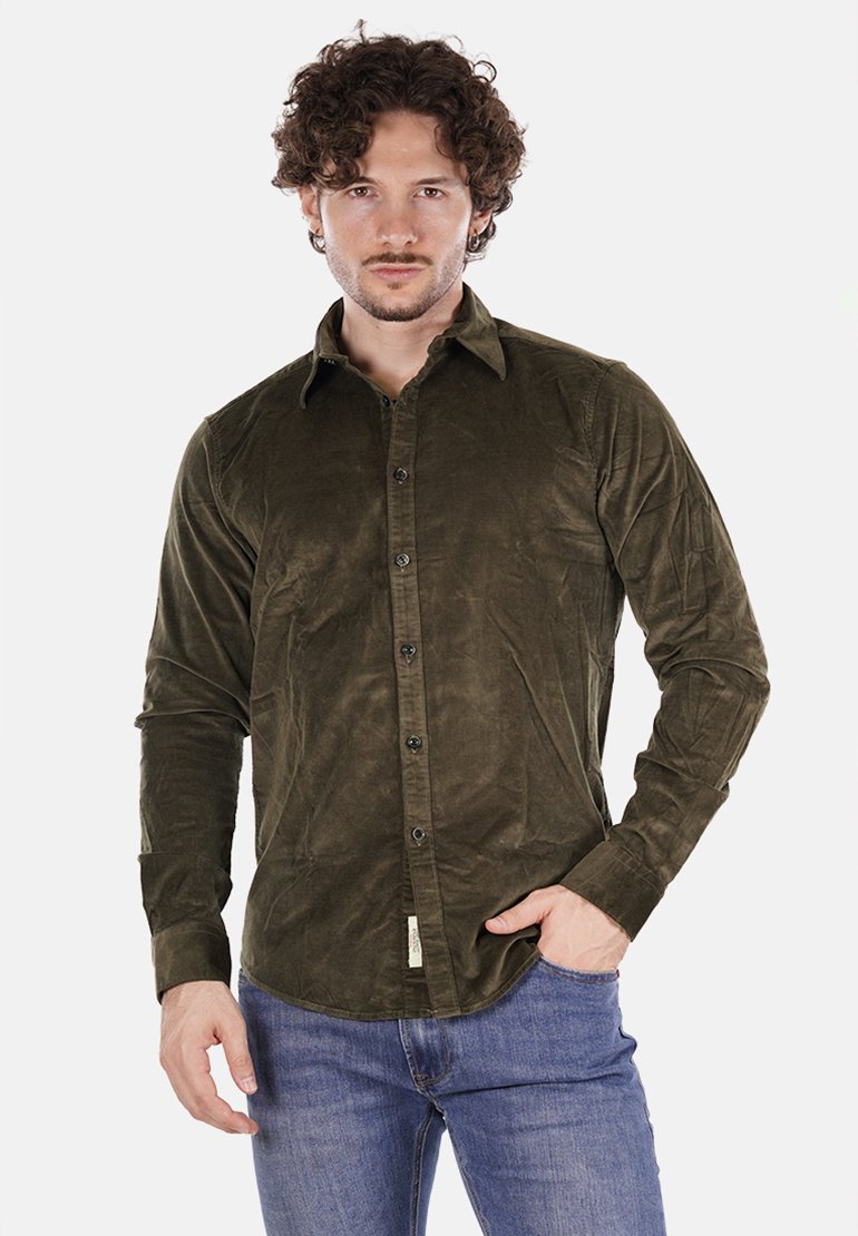 Camicia di corduroy verde oliva con maniche lunghe, colletto bottonato e bottoni neri. Abbinata a jeans blu, che mostrano una texture liscia.