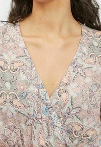 Flerfärgad, mönstrad blus med V-ringning. Tyget har intrikata paisleymotiv i mjuka pastellfärger. Slät textur.