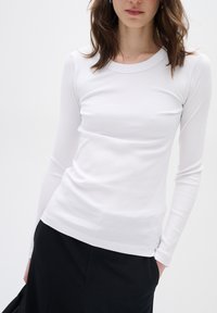 Vit långärmad ribbad topp med rund halsringning. Mjuk textur, åtsittande siluett, kombinerad med en svart kjol. Minimalistisk design.