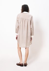 Gestreiftes, übergroßes Hemdkleid in Beige, Creme und Rost, mit langen Ärmeln, einem Rückenschlitz und abgerundetem Saum, kombiniert mit braunen Schuhen.