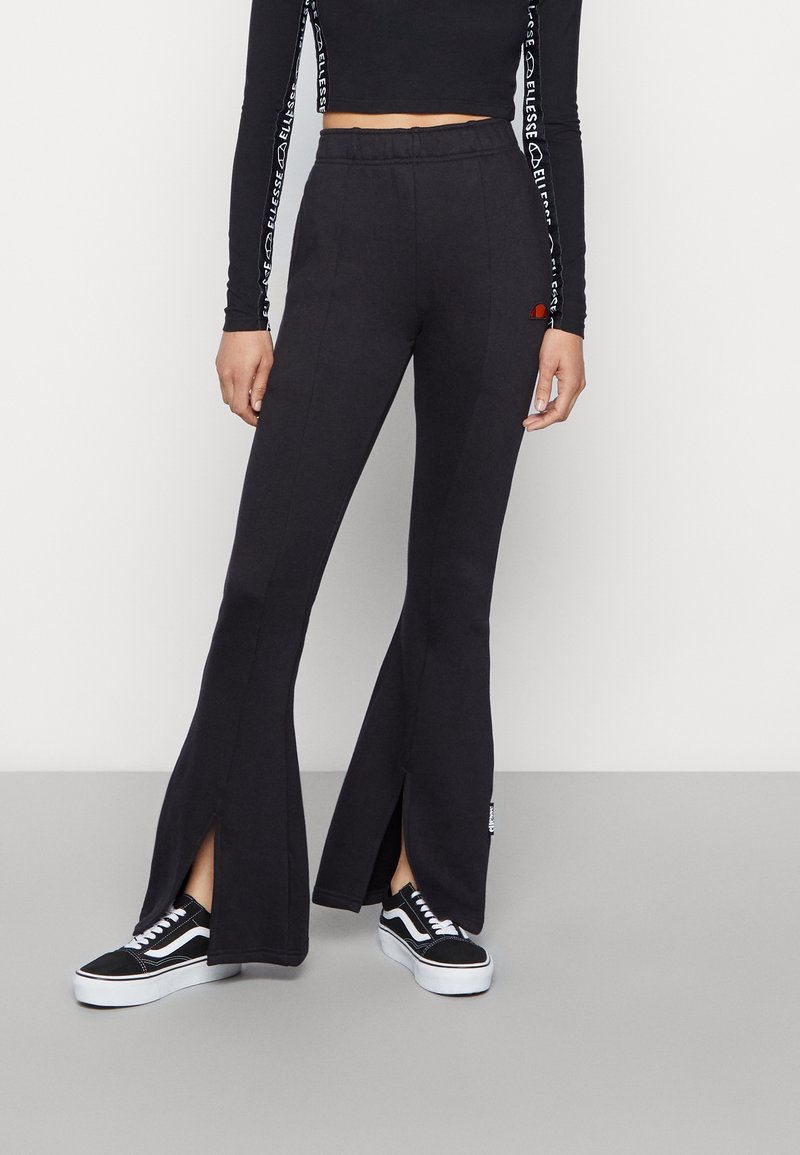 Svart flare-byxor i mjukt material, med sidoflikar vid fållen och en logodetalj. Matchas med svarta sneakers.