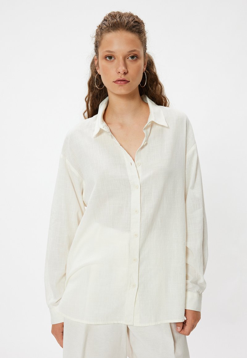 Lekka, off-white koszula z guzikami o luźnym kroju, długich rękawach i kołnierzyku. Cechuje się delikatną fakturą i subtelną przezroczystością.