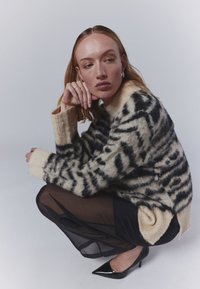 Overmaatse crème en zwarte gestreepte trui in een donzige textuur, gecombineerd met een zwarte doorschijnende rok en puntige zwarte hakken.