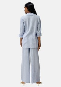 Lichtblauwe, textuurstof set bestaande uit een lange blouse en een broek met wijde pijpen. De blouse heeft opgerolde mouwen; beide stukken hebben een ontspannen pasvorm.