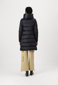 Black puffer coat with a high collar, ribbed texture, and quilted design. Paired with light-colored cargo pants and black boots.