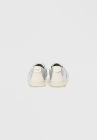 Adidași gri și albi cu un superior din piele netedă și textile, vârful rotund, sistem de închidere cu șnururi și un logo embosat subtil pe călcâi.
