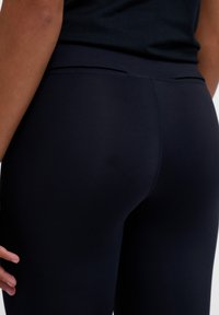 Sorte svarte treningsleggings laget av et glatt, elastisk stoff. Har høy midje og tettsittende design uten synlige logoer eller mønstre.