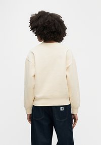 Φόρμα σε ανοιχτό μπεζ χρώμα με στρογγυλή λαιμόκοψη, ραμμένα ώμους και ριμπ τελείωμα, συνδυασμένη με σκούρο τζιν παντελόνι με λογότυπο πλακέτα.