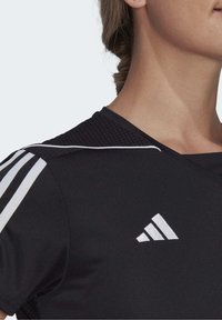 Camiseta deportiva negra con un diseño texturizado en los hombros, rayas blancas como acento y un logo blanco en el pecho. Material suave, corte ajustado.