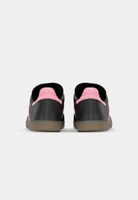 Sorte og lyserøde retro sneakers med en struktureret overflade, der har en lav profil, polstret krave og en gummisål for bedre trækkraft.