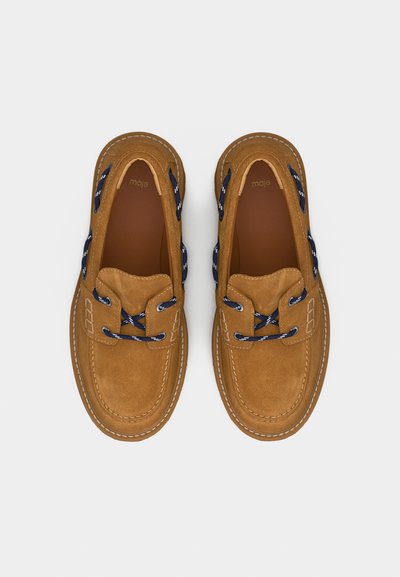 Paire de chaussures bateau en suède marron avec des lacets bleu marine et blancs, des coutures visibles et des semelles intérieures marron lisses portant la marque "maje".