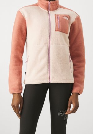 Hellrosa und pfirsichfarbene Fleecejacke mit durchgehendem Reißverschluss, Brusttasche und Seitentaschen, getragen mit schwarzen Leggings mit weißem Schriftzug.