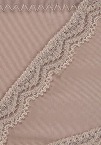 Tessuto beige con una trama liscia presenta un delicato bordo in pizzo grigio chiaro e cuciture a zigzag, evidenziando dettagli intricati.