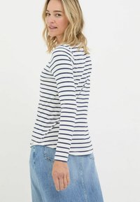 Long-sleeve shirt with navy stripes on a white background, made of soft fabric; rounded hem and a relaxed fit. Worn with a denim skirt.