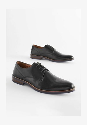 Mustad musta nahast kingad sileda viimistlusega, paeltega disain, ümar varvas ja kontrastsest pruunist tallast. Servad on õmmeldud.