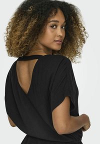 Vêtement noir à manches courtes, doté d'une encolure en V et d'une découpe dans le dos. Tissu texturé. Présente une coupe décontractée, mettant en avant le confort et le style.