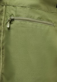 Κοντινό πλάνο μιας τσέπης πράσινου υφάσματος με οριζόντια φερμουάρ και ταινία τραβήγματος σε ένδυμα.