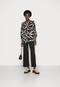 Blusa abstrata com padrão preto e rosa, com mangas de três quartos, combinada com calças largas pretas com pregas e sapatos de slip-on bege.