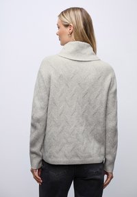 Pull gris clair à texture côtelée, avec un col montant et un motif en zigzag dans le dos. Coupe décontractée et manches longues.