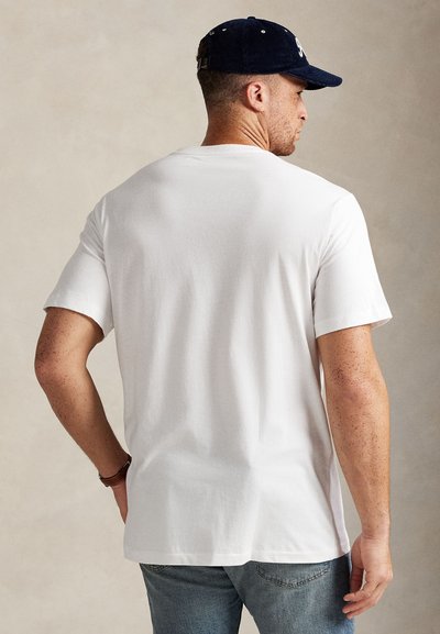 Bílé triko s krátkými rukávy, volným střihem, jemnou texturou a rovnými lemy, doplněné modrými džínami a tmavě modrou čepicí.