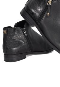 Pair of black ankle boots with mixed smooth and textured leather, side zippers, low heels, and gold zipper pulls on white background.