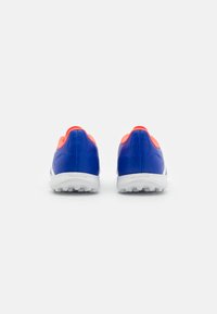 Chaussures de sport bleu et orange avec une tige en synthétique lisse, un talon arrondi, des accents texturés et une semelle en caoutchouc blanc avec des crampons d'adhérence.