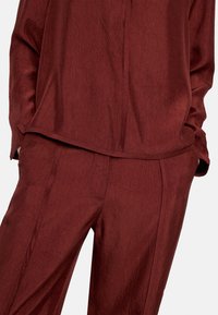Bordowy strój wykonany z fakturowanej tkaniny. Bluzka ma luźny krój, natomiast spodnie są taliowane z prostą nogawką i subtelnymi zagnieceniami.