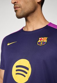 Barcelona football jersey in purple with pink accents, featuring a yellow Spotify logo and embroidered club crest. Textured fabric design.