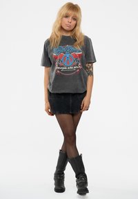 Gray graphic t-shirt with blue and red logo text "Aerosmith Deuces Are Wild," paired with a black denim skirt and black ankle boots.