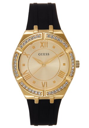 Goudkleurig Guess-horloge met zwarte siliconen band, bezel bezet met kristallen, Romeinse cijfers en drie gouden wijzers die 7:11:36 aangeven.