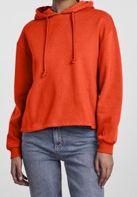 Röd huvtröja i mjukt bomullstyg. Har dragsko, långa ärmar och en avslappnad passform, tillsammans med blå jeans.