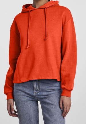 Czerwona bluza z kapturem wykonana z miękkiej bawełny. Posiada sznurki, długie rękawy i luźny krój, zestawiona z niebieskimi dżinsami.