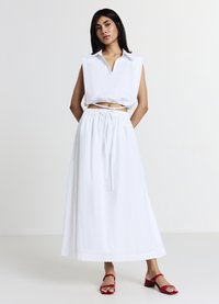 Blusa bianca senza maniche con scollatura a V, abbinata a una lunga gonna bianca con vita elastica e cordino. Sandali con tacco rossi.